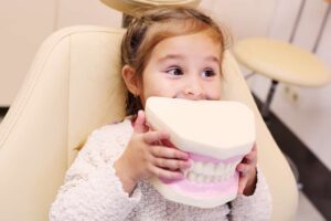 nena somrient asseguda a la cadira dental amb mandíbula artificial a les mans